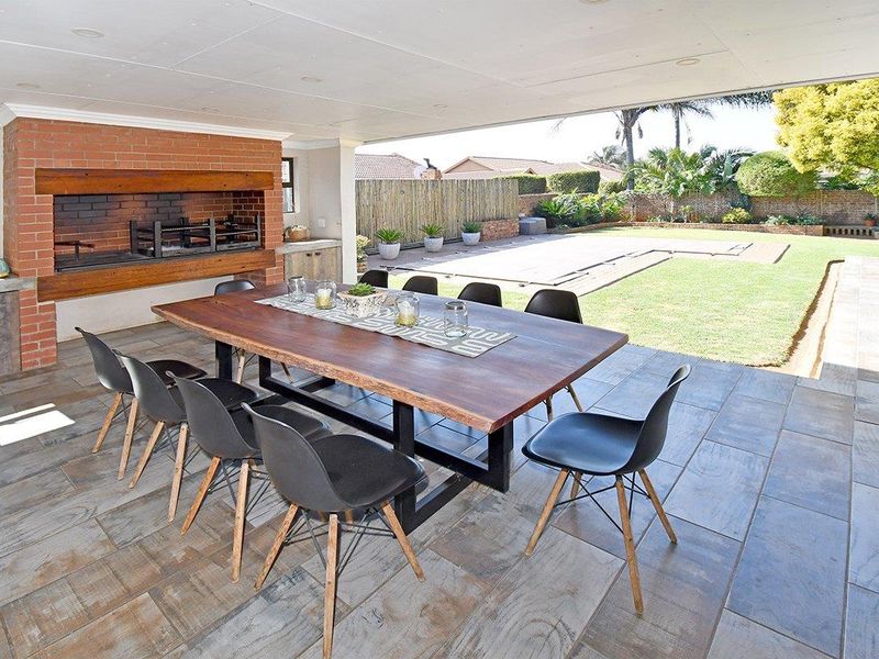 Spacious covered patio featuring a built-in brick braai, tiled flooring, and direct access to the garden and pool area.