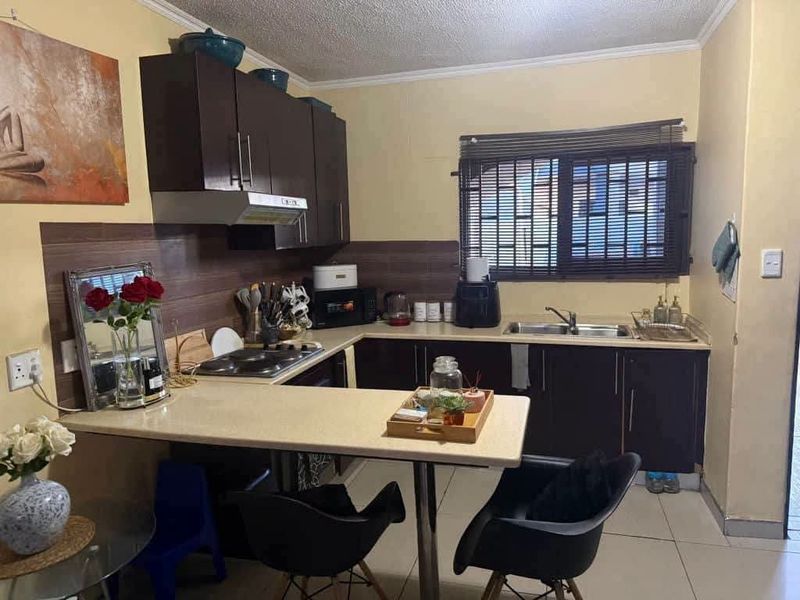 A functional kitchen featuring dark cabinetry, laminate countertops, a built-in electric hob with extractor, and tiled flooring.