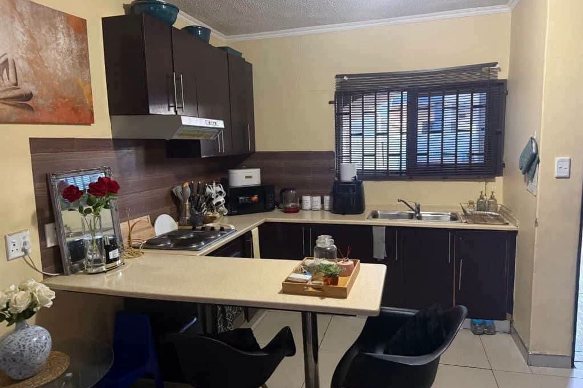 A functional kitchen featuring dark cabinetry, laminate countertops, a built-in electric hob with extractor, and tiled flooring.