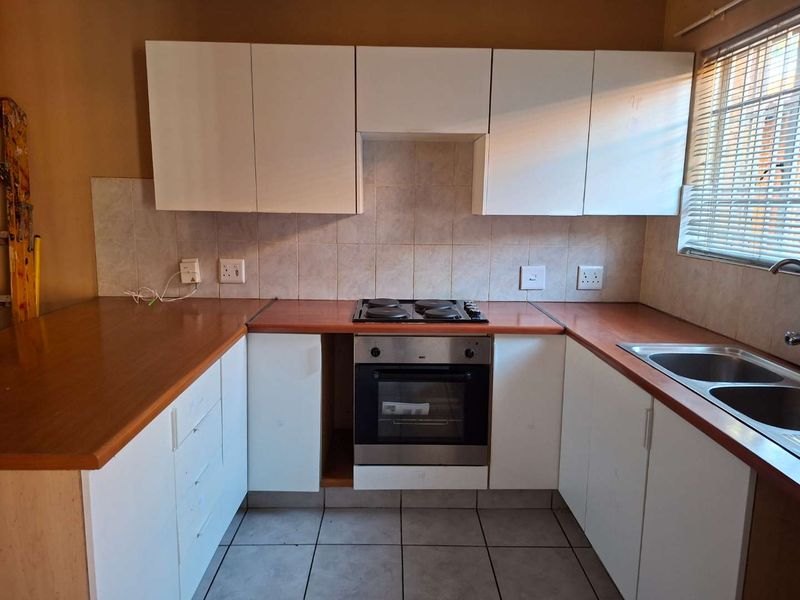 A functional kitchen featuring white cabinetry, laminate countertops, a built-in oven with electric hob, and a double bowl sink with tiled backsplash.