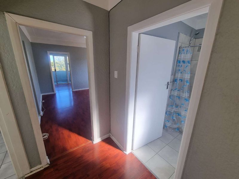 A functional hallway connecting to a bedroom and a bathroom with a shower, featuring laminate flooring and neutral wall tones.