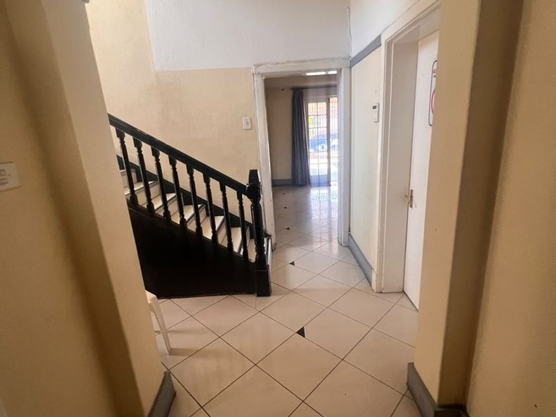A spacious entrance hallway featuring tiled flooring, a classic staircase with a dark wooden balustrade, and an arched entryway leading to the living area.