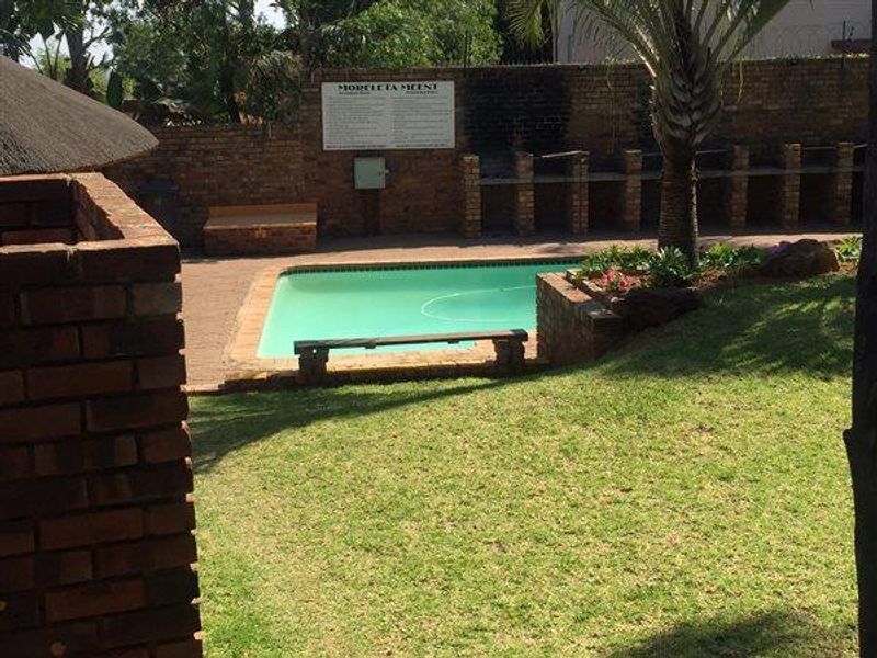 Communal pool area featuring a swimming pool, paved surround, built-in braai facilities, and a brick boundary wall within a landscaped garden setting.