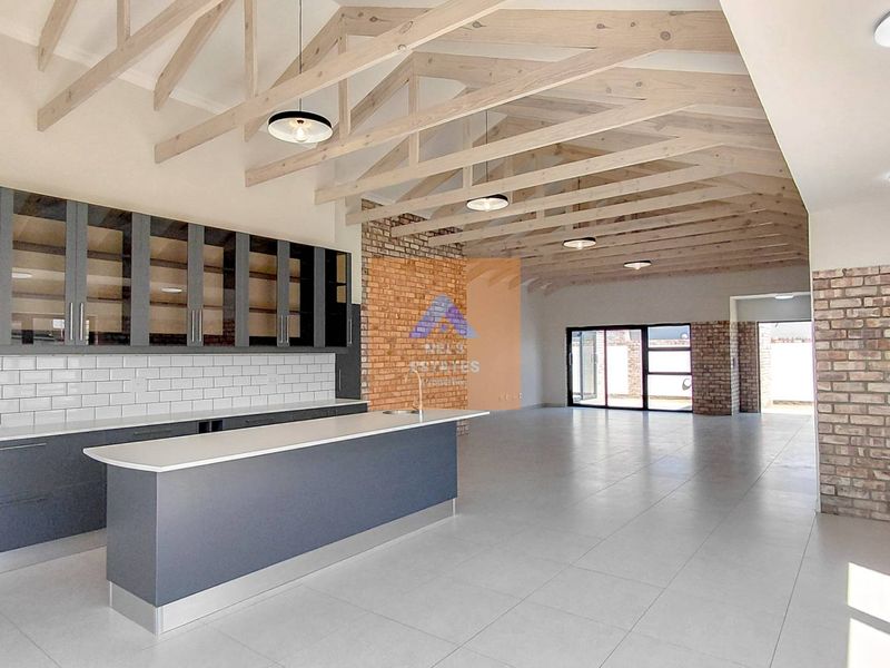 Spacious open-plan living area featuring exposed timber trusses, a brick feature wall, and a modern kitchen with a central island and subway tile backsplash.