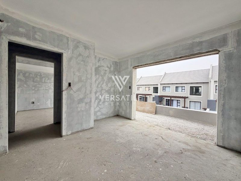 An unfinished interior living space in a townhouse, featuring raw plastered walls, exposed wiring, and a large opening leading to an outdoor balcony area.
