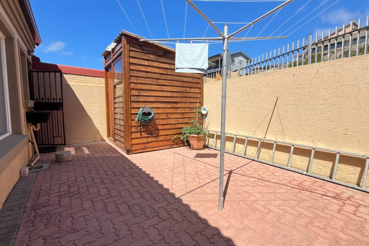 A paved rear courtyard area featuring a wooden storage shed, perimeter boundary walls, and a rotary clothesline.