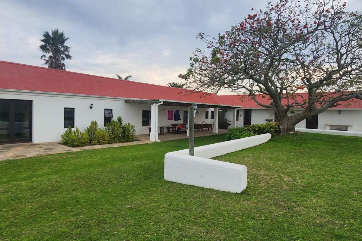 A rear view of the farm property featuring a red corrugated roof, a covered patio area, and a well-maintained lawn with mature landscaping.