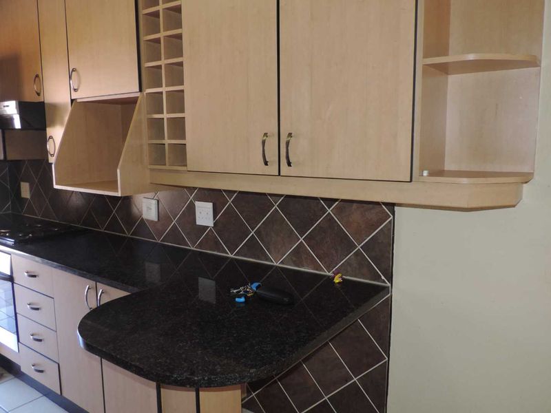 A functional kitchen featuring light wood cabinetry, dark granite countertops, a built-in oven with gas hob, and a decorative tiled backsplash.