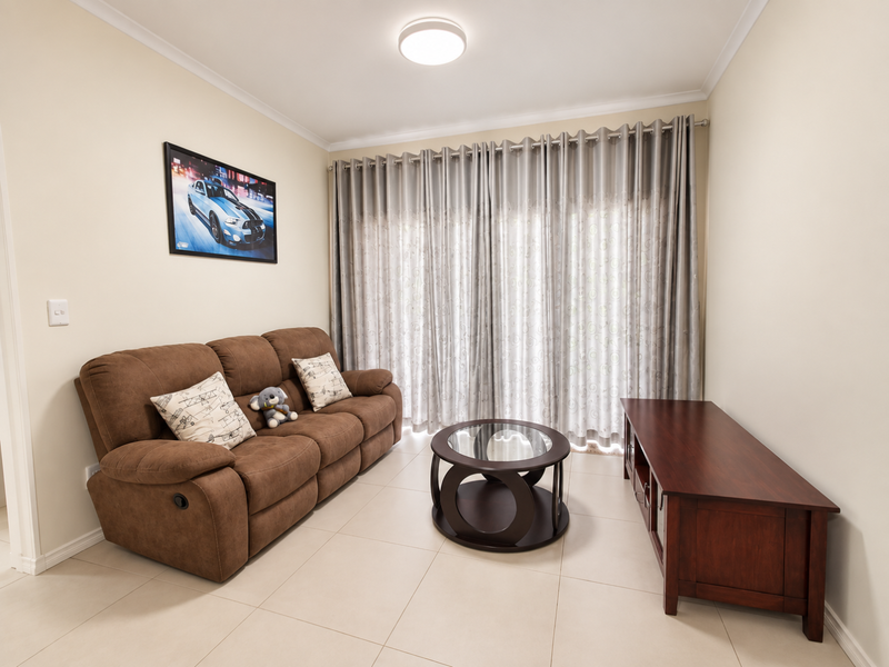 A well-maintained living room featuring neutral tiled flooring, a ceiling light fixture, and large sliding glass doors with installed curtain tracks.