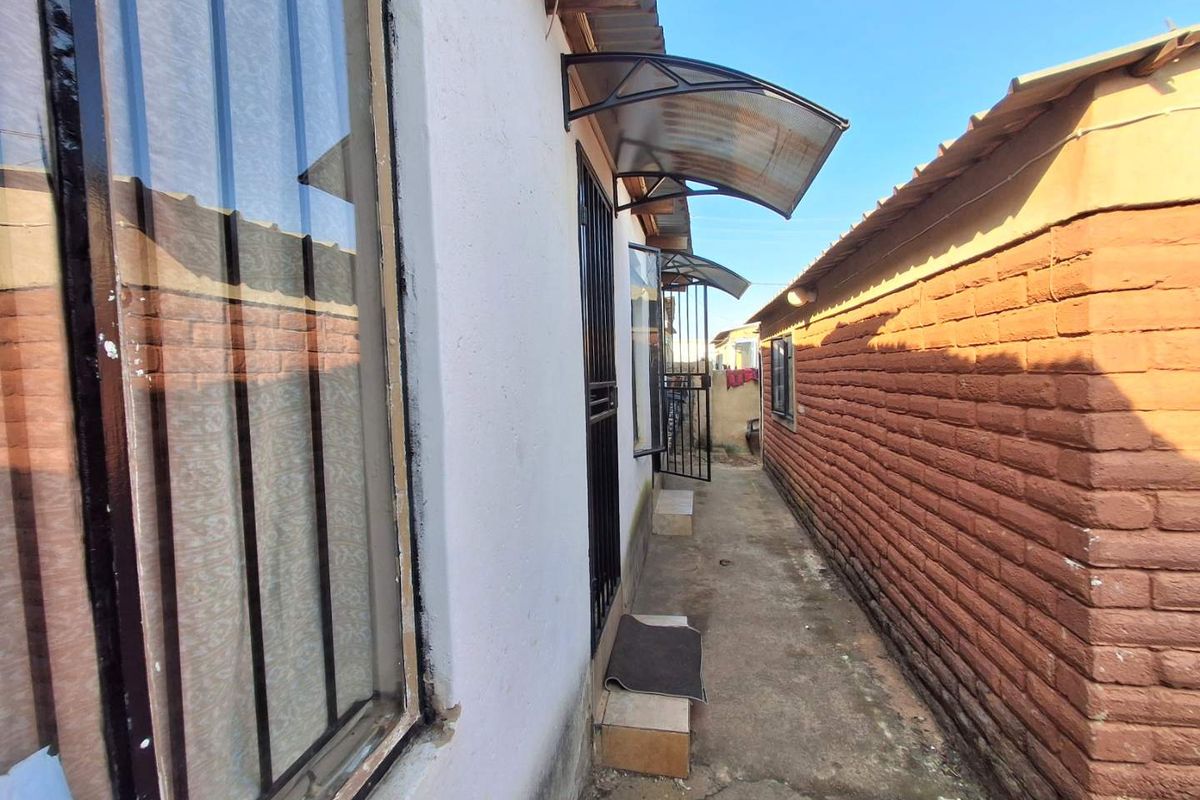 A narrow side passage between the main house and a brick boundary wall, featuring security bars and protective door awnings.