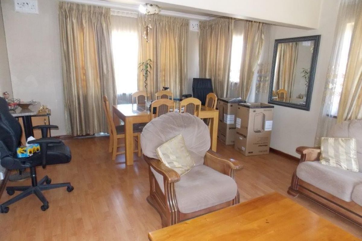 A living room area featuring laminate flooring and large windows with curtain rails, offering a functional space for relaxation and dining.