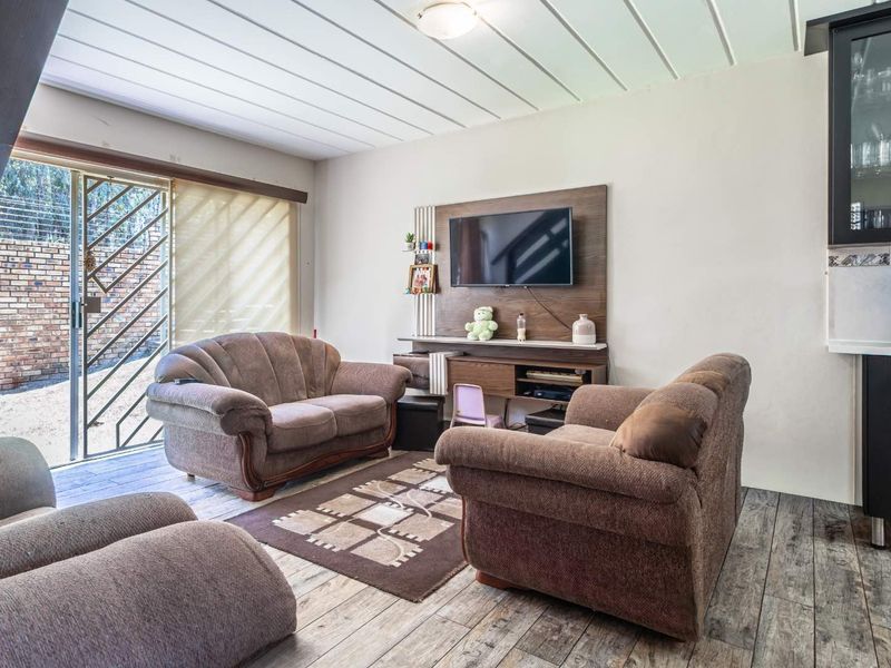 A living room featuring wood-look tile flooring, a built-in media unit, and a sliding glass door with a security gate leading to the exterior.