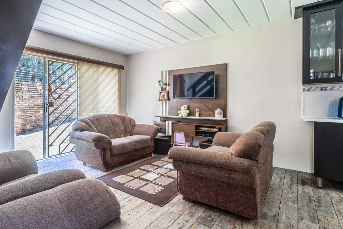 A living room featuring wood-look tile flooring, a built-in media unit, and a sliding glass door with a security gate leading to the exterior.
