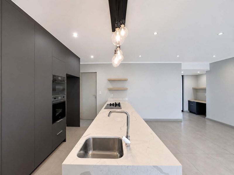 Modern kitchen featuring a large stone-topped island with an undermount sink, built-in appliances, sleek cabinetry, and minimalist floating shelves.
