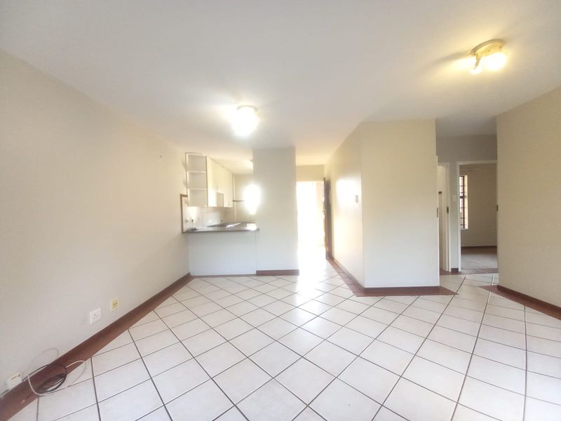 An open-plan living and kitchen area featuring neutral tiled flooring and built-in cabinetry, offering a blank canvas for interior design.