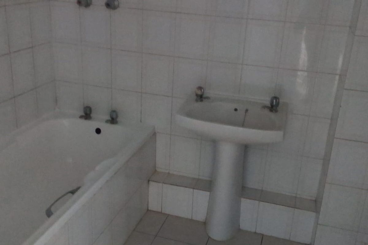 A dated bathroom featuring a pedestal washbasin, built-in bathtub, and toilet with white ceramic wall and floor tiles.
