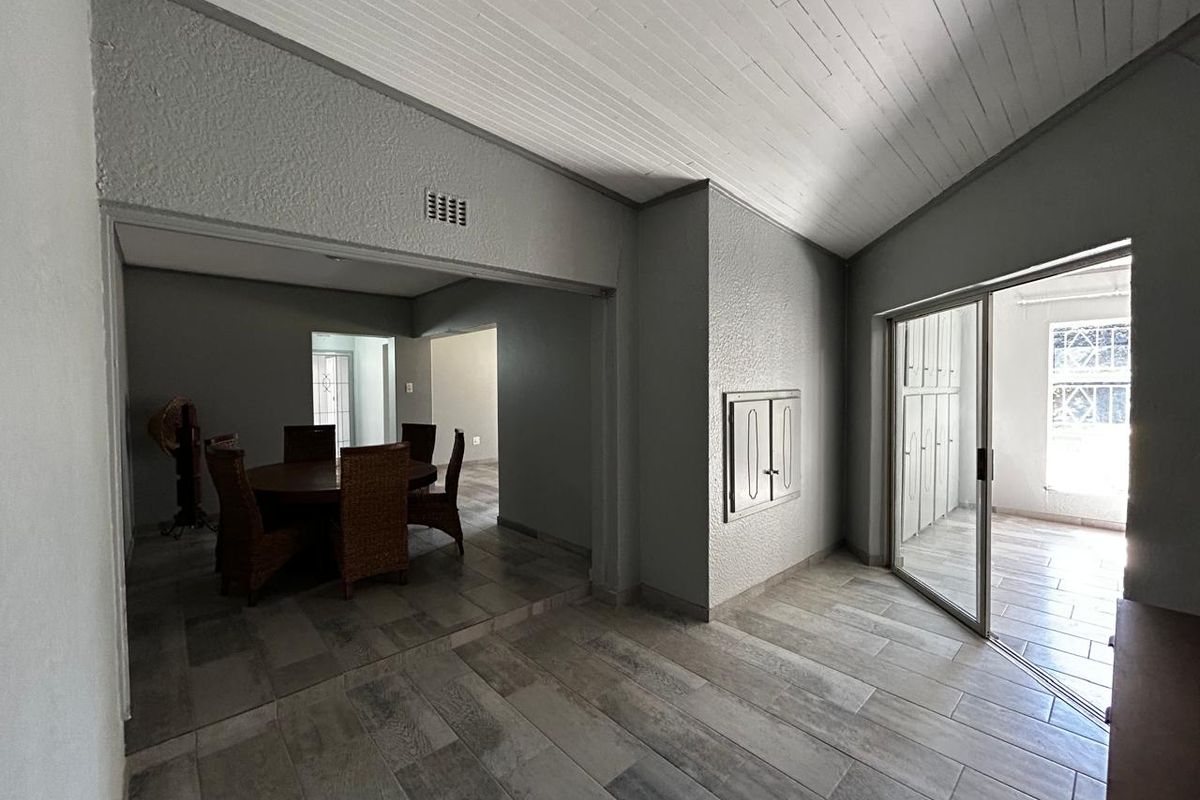 Spacious living area featuring tiled flooring, a vaulted ceiling, and a sliding glass door providing access to an outdoor patio space.