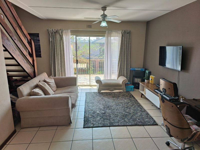A living room featuring tiled flooring, a ceiling fan, and a wooden staircase, with sliding glass doors providing access to a balcony.