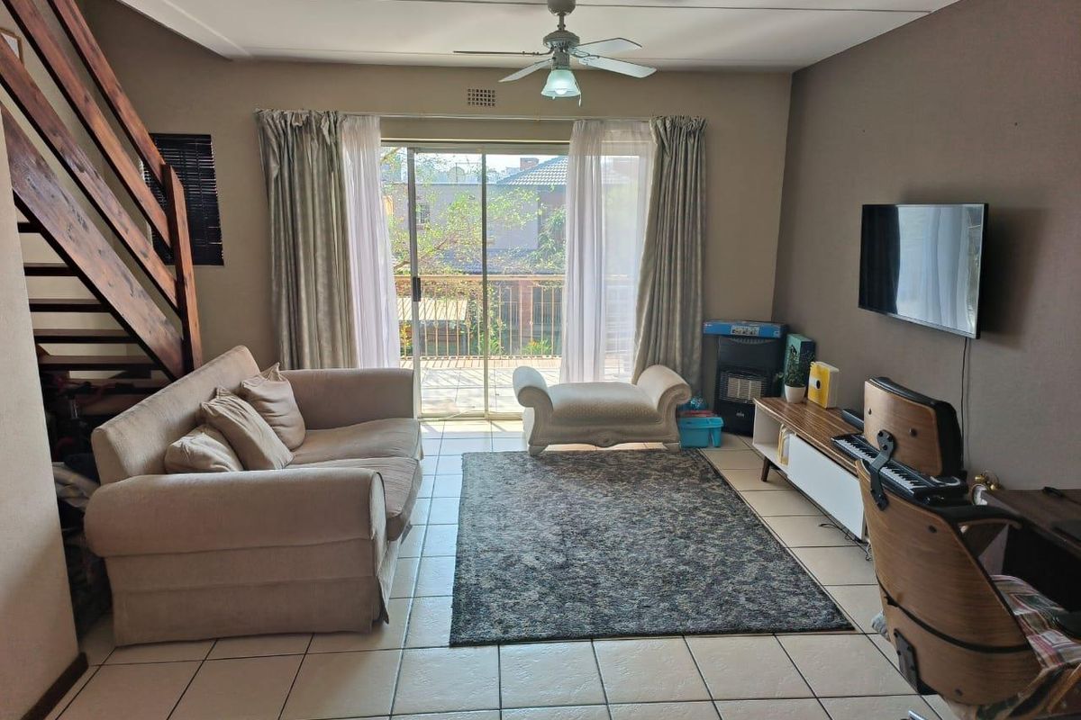 A living room featuring tiled flooring, a ceiling fan, and a wooden staircase, with sliding glass doors providing access to a balcony.
