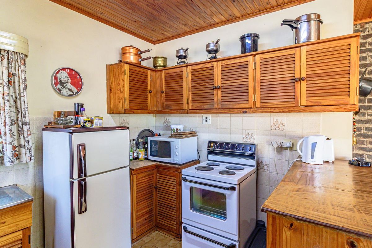 A compact kitchen featuring timber cabinetry, a tiled backsplash, a freestanding stove, and a timber-paneled ceiling.