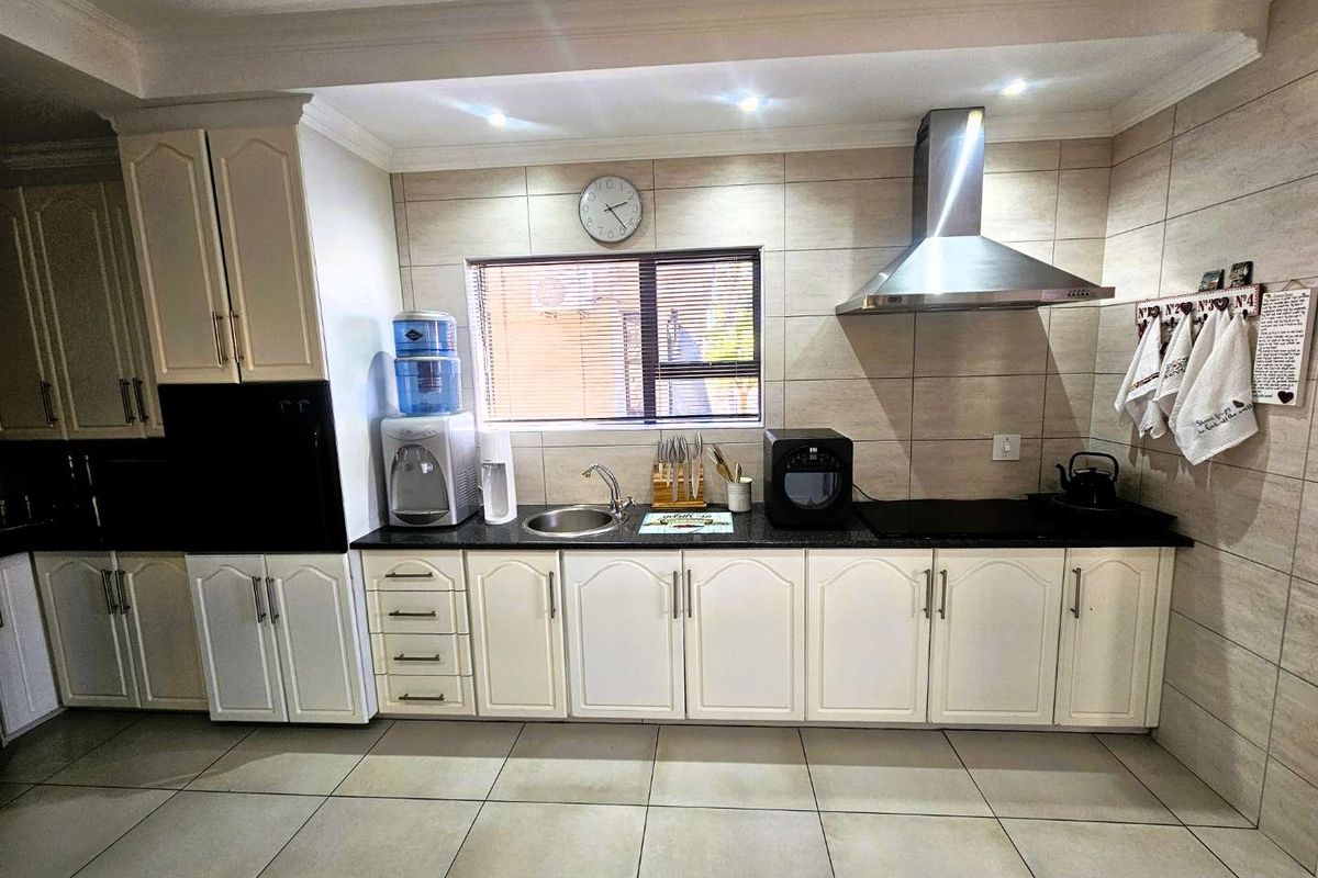 A well-maintained kitchen featuring white cabinetry, granite countertops, a stainless steel extractor fan, and tiled flooring with a functional layout.