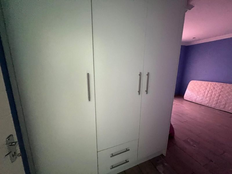 A bedroom featuring a white built-in wardrobe with integrated drawers and laminate flooring.