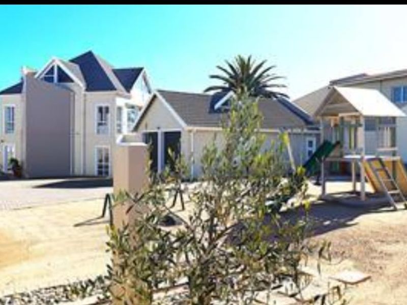 Rear view of the property featuring a paved driveway, double garage, and landscaped garden area.