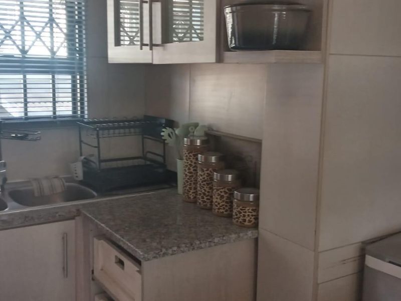 A functional kitchen area featuring laminate countertops, double bowl stainless steel sink, and built-in cabinetry with security bars on the window.