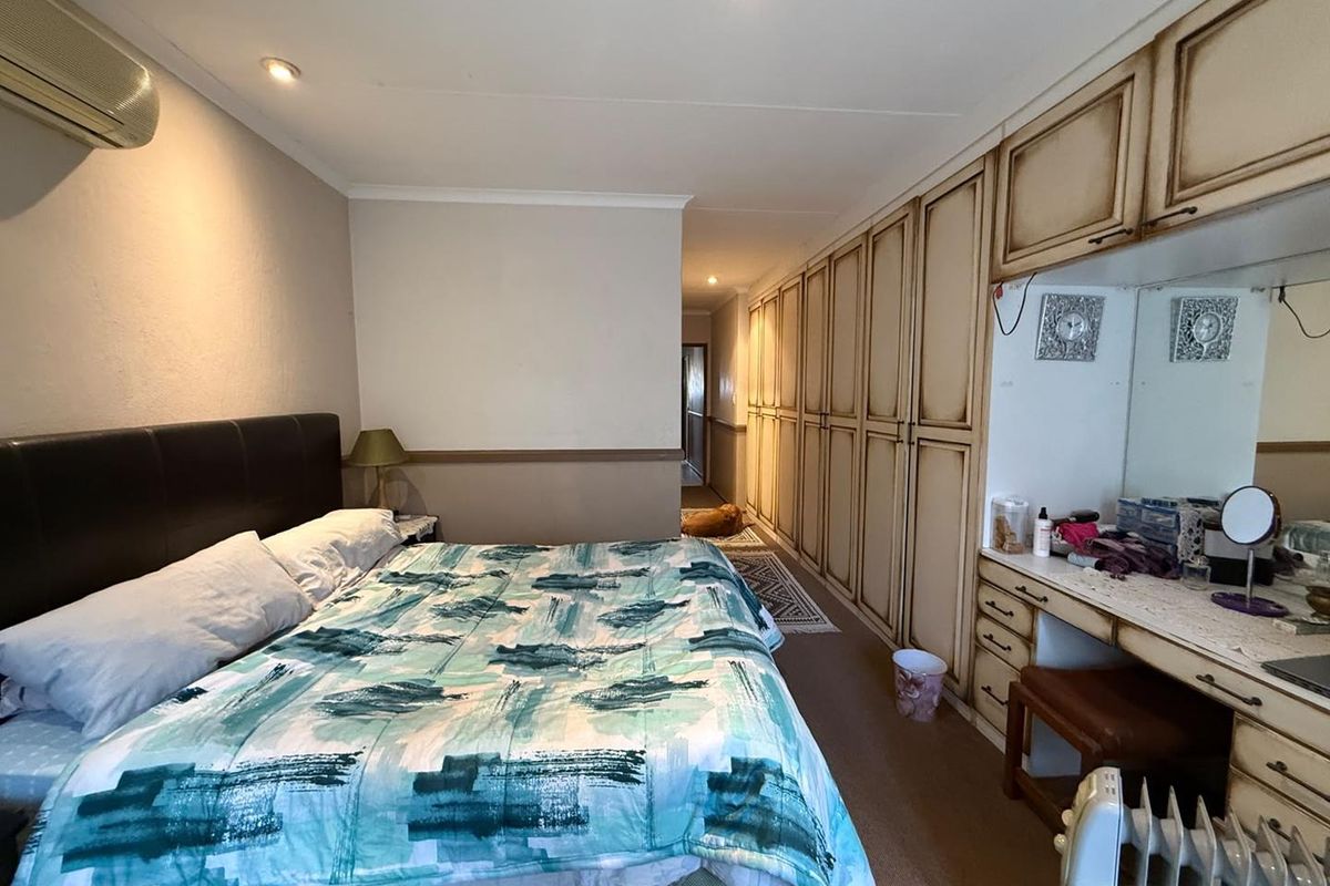 Spacious bedroom featuring extensive built-in cabinetry, a dedicated vanity area, and a wall-mounted air conditioning unit.