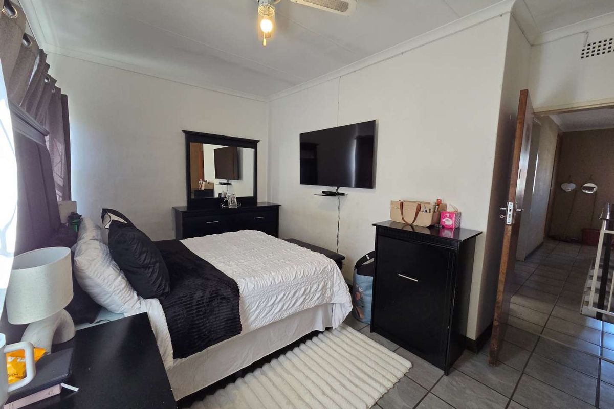 A bedroom featuring tiled flooring, a ceiling fan, and a wall-mounted television setup.