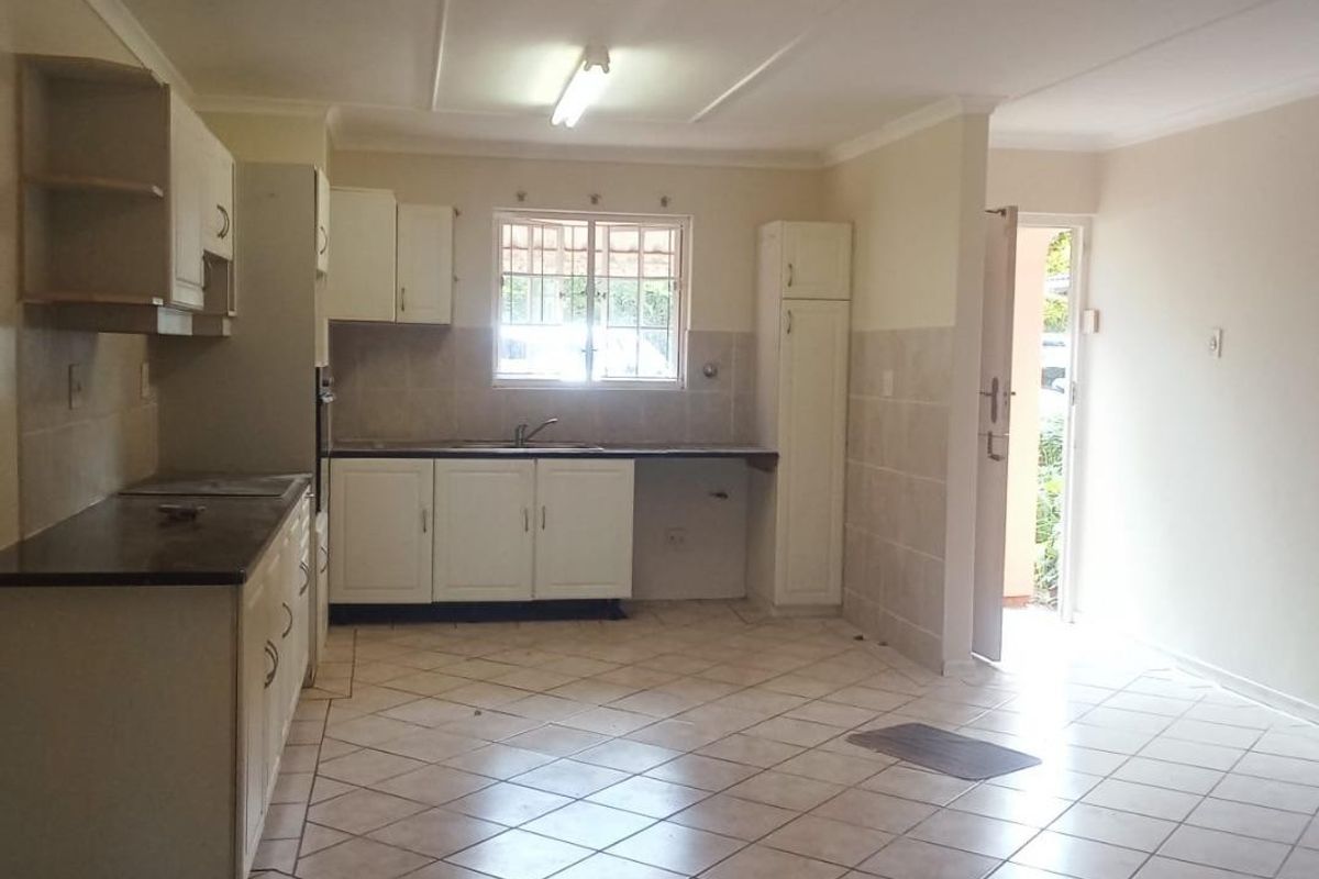 A functional kitchen featuring tiled flooring, built-in cabinetry with laminate countertops, and a stainless steel sink, with direct access to the exterior.