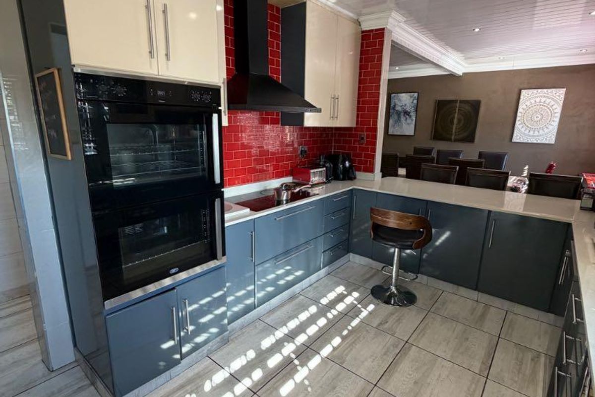 Modern kitchen featuring two-tone cabinetry, a striking red tiled backsplash, built-in double oven, extractor fan, and a breakfast bar counter.