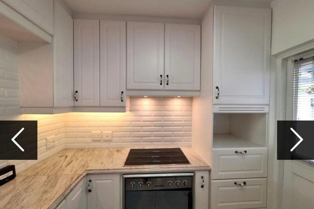 A clean, modern kitchen featuring white cabinetry, stone countertops, a subway tile backsplash, and integrated appliances including an electric hob and oven.