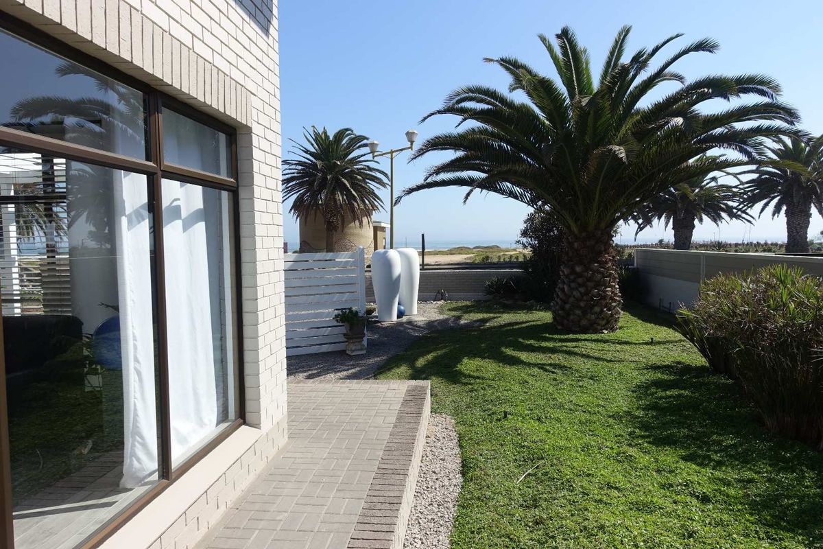 A well-maintained rear garden featuring a paved walkway, manicured lawn, and established palm trees, offering a pleasant outdoor space with a coastal view.