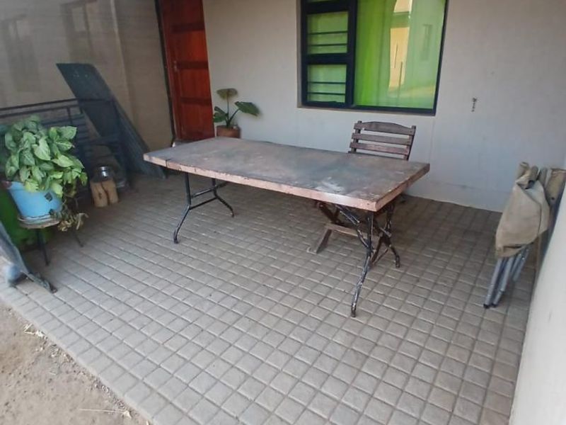 A covered outdoor patio area featuring tiled flooring, a corrugated metal roof, and direct access to the home via a timber door.