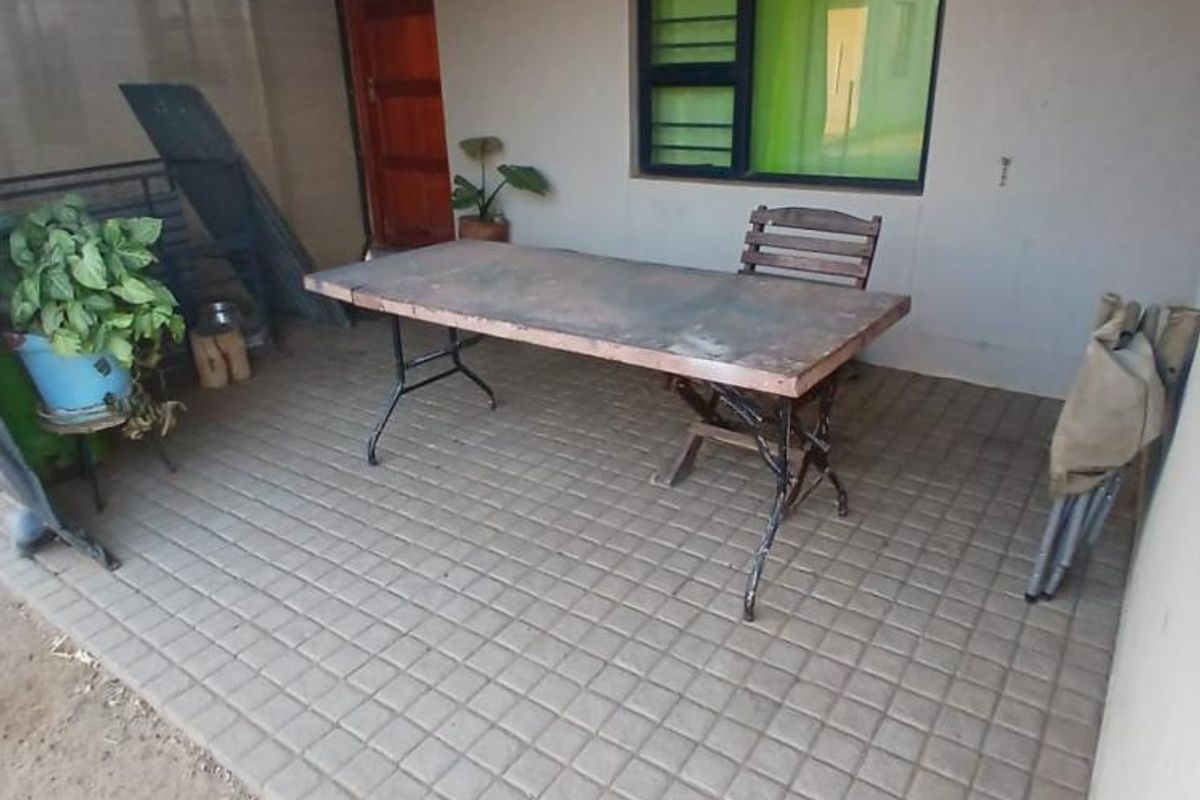 A covered outdoor patio area featuring tiled flooring, a corrugated metal roof, and direct access to the home via a timber door.