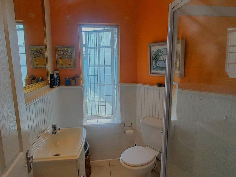 A functional bathroom featuring a vanity basin, toilet, and shower enclosure with wainscoting wall paneling and a security gate on the window.