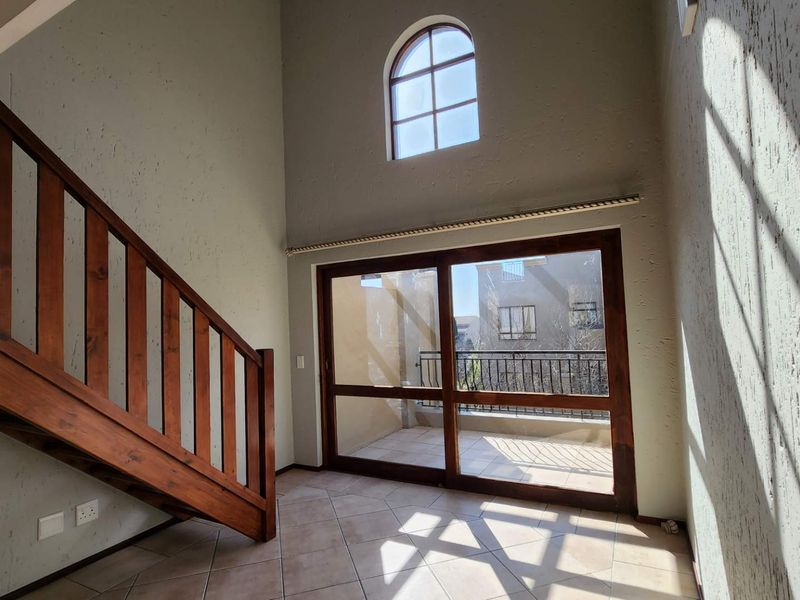An empty living area featuring a wooden staircase, high ceilings with an arched window, and large sliding doors leading to a balcony.