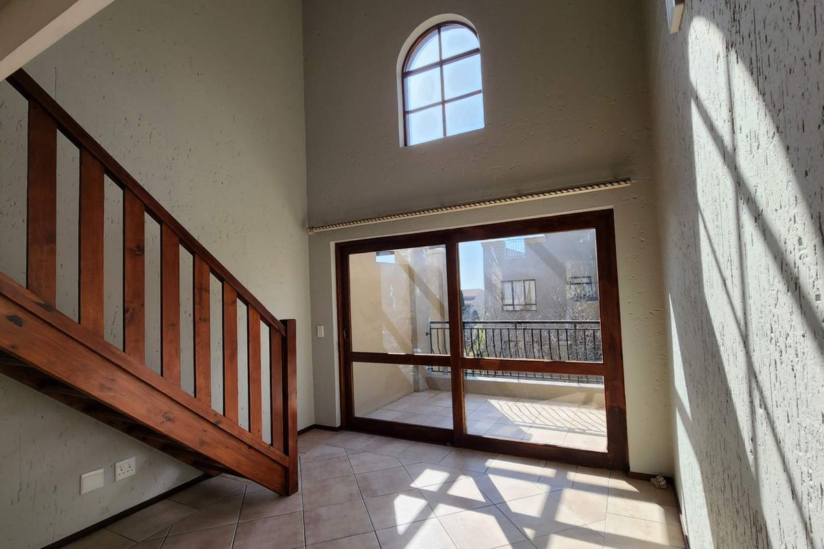 An empty living area featuring a wooden staircase, high ceilings with an arched window, and large sliding doors leading to a balcony.