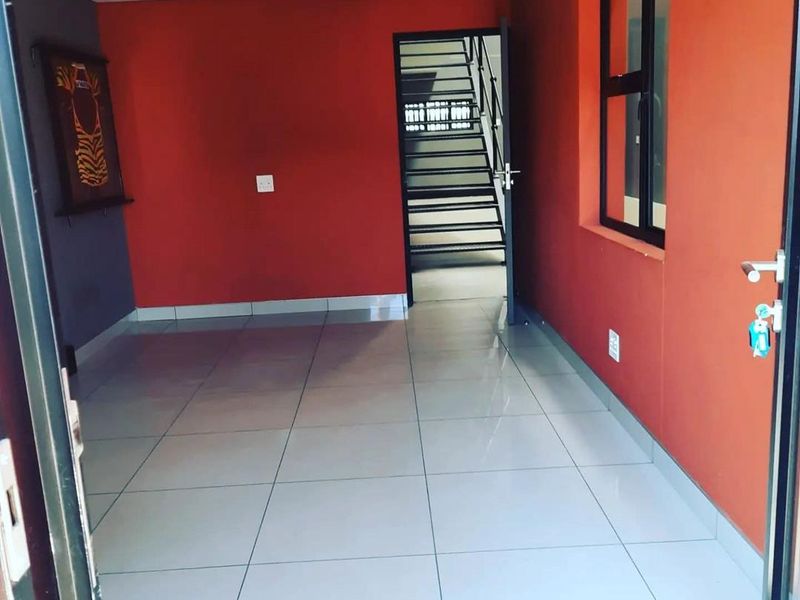 A clean, empty office space featuring tiled flooring, recessed lighting, and an internal staircase leading to an upper level.