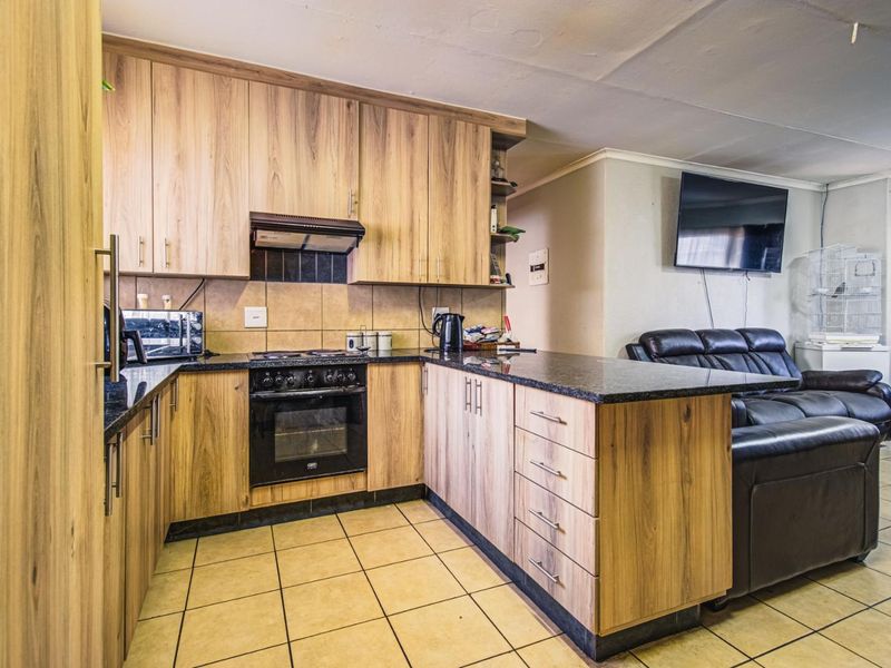 Open-plan kitchen featuring wood-look cabinetry, granite countertops, and integrated appliances, flowing directly into the adjacent living area with tiled flooring throughout.