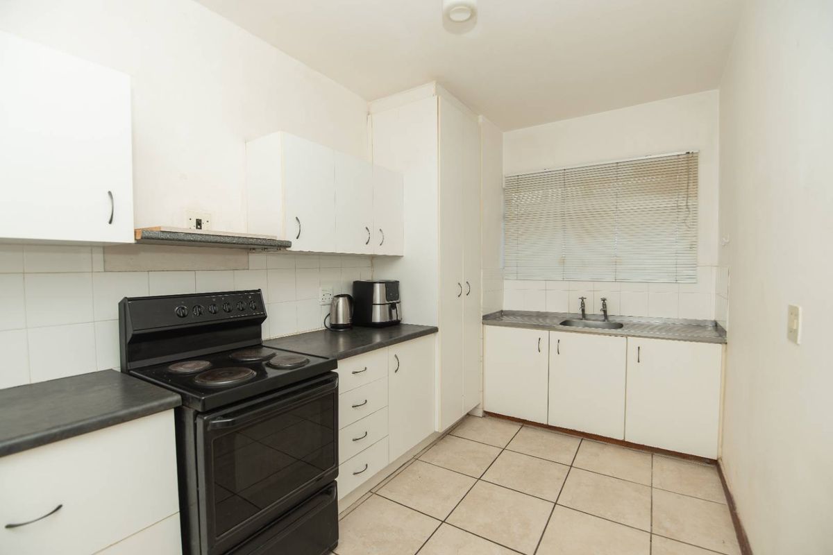 A functional kitchen featuring white cabinetry, laminate countertops, a stainless steel sink, and tiled flooring, offering a clean and practical layout.
