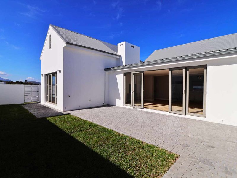 Modern rear exterior featuring a paved patio, manicured lawn, and large sliding glass doors leading into the home.