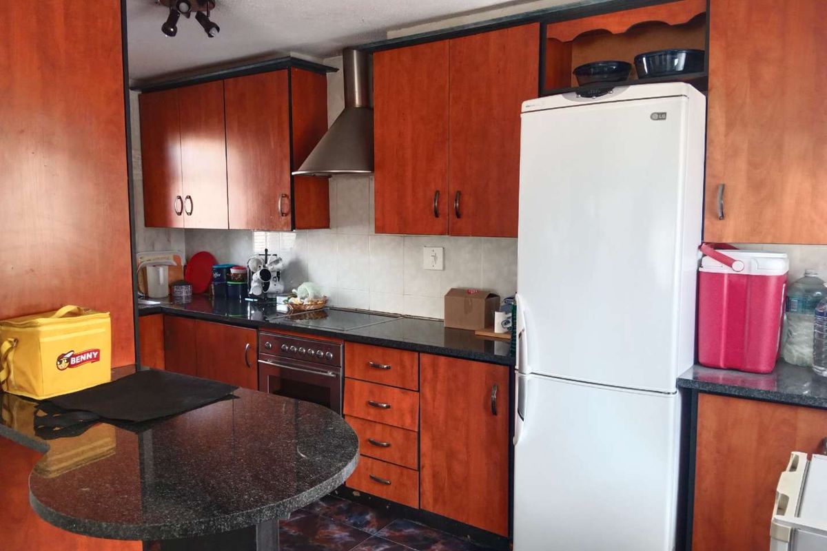 A functional kitchen featuring wood-finish cabinetry, granite countertops, a built-in oven with extractor fan, and tiled flooring.