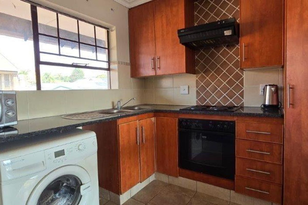 Functional kitchen featuring wooden cabinetry, granite countertops, built-in oven with extractor fan, and tiled backsplash, offering a practical layout for daily use.