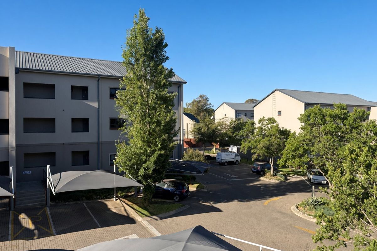 An elevated view of the apartment complex exterior, featuring paved parking areas with shade cloth carports and well-maintained building facades.