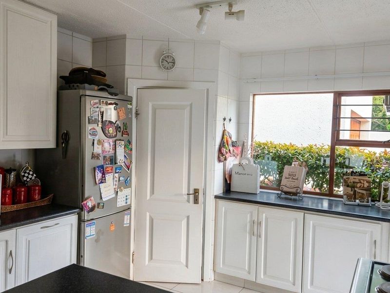 A functional kitchen featuring white cabinetry, dark countertops, tiled backsplash, and a window overlooking the garden area.