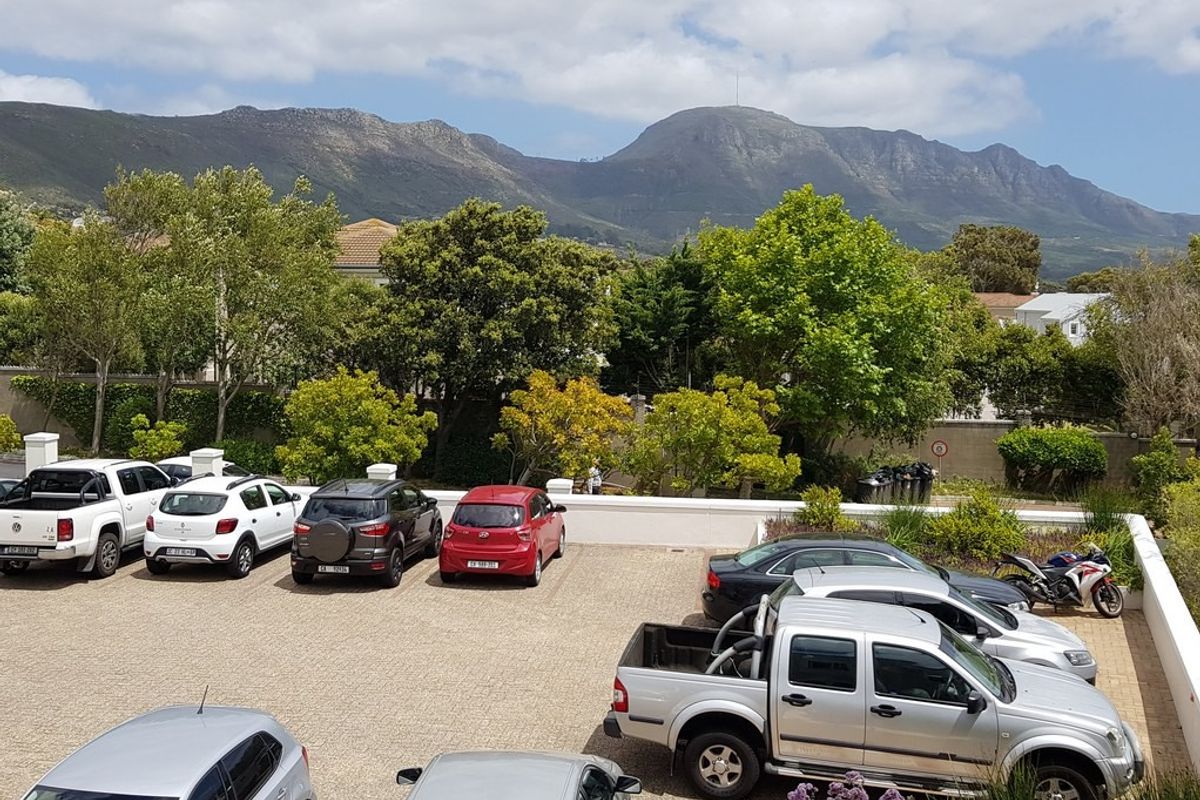 An elevated view of a paved parking area featuring a boundary wall and mature trees, set against a scenic mountain backdrop.