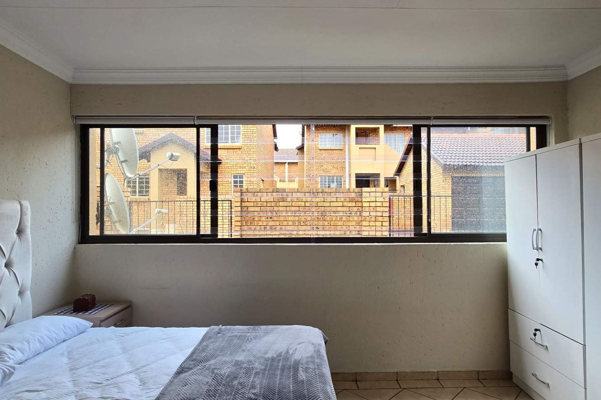 A bedroom featuring tiled flooring, textured walls, and a large window providing natural light and views of the surrounding townhouse complex.