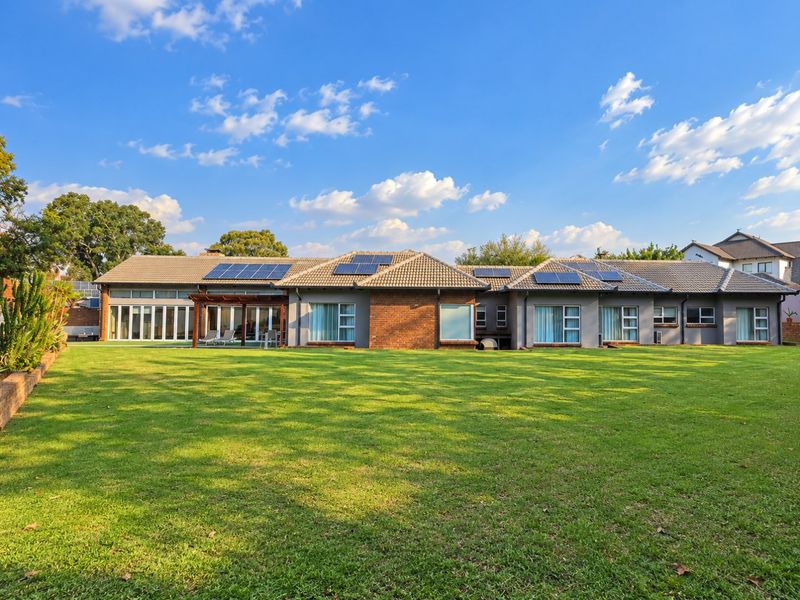 Spacious rear exterior view of a well-maintained house featuring a large lawn, solar panels, and a covered patio area with sliding glass doors.